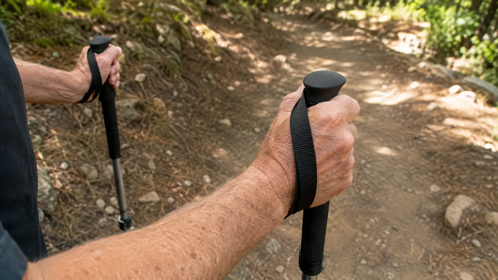 A hand gripping a foam trekking pole handle on a trail